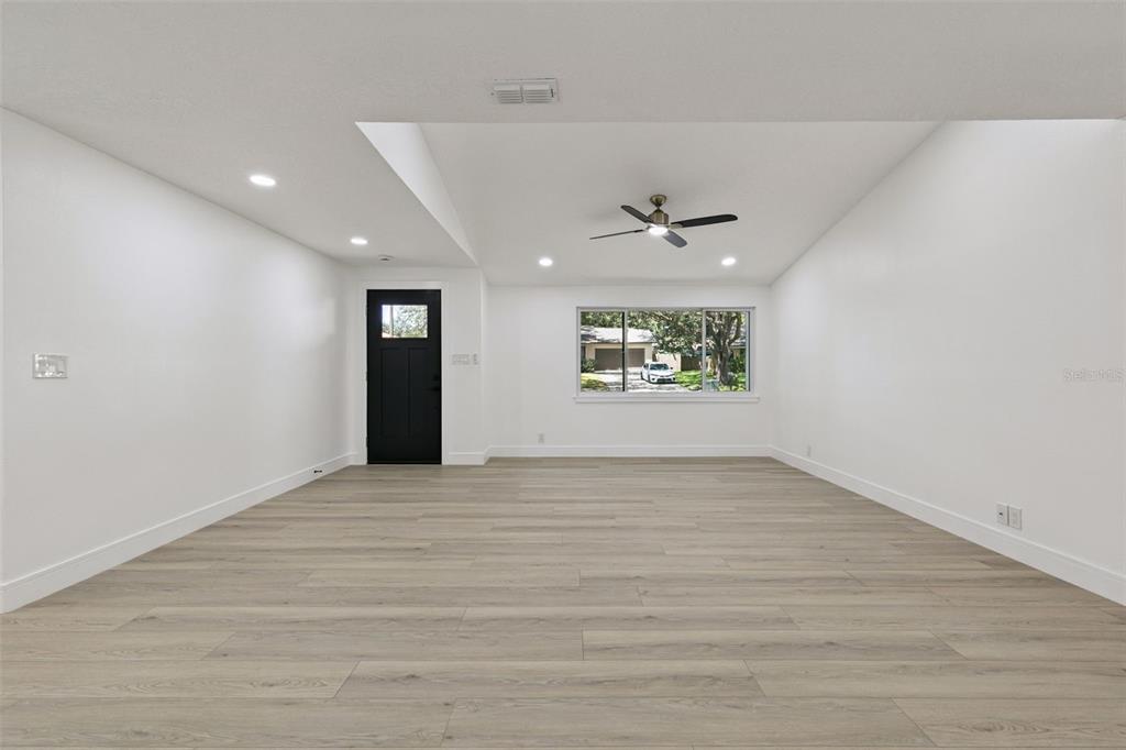A bright, empty living room features white walls, light wood-look flooring, and a black door — 141 MILL RUN DRIVE, LAKE MARY, FL