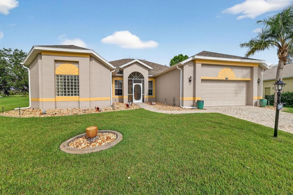 A tan single-story house with a two-car garage and a glass block window feature — 3606 MULBERRY GROVE LOOP, LEESBURG, FL