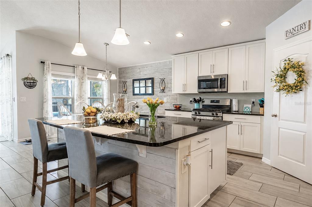 A kitchen features white cabinets, a black granite island, and light wood-look tile flooring — 1510 CHELSEA MANOR CIRCLE, DELAND, FL