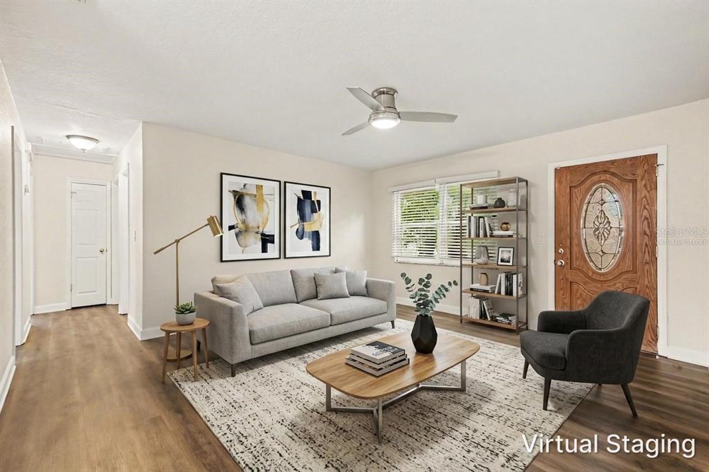 A living room with wood-look flooring, a gray sofa, an armchair, and a wooden front door — 2051 23RD STREET SW, LARGO, FL