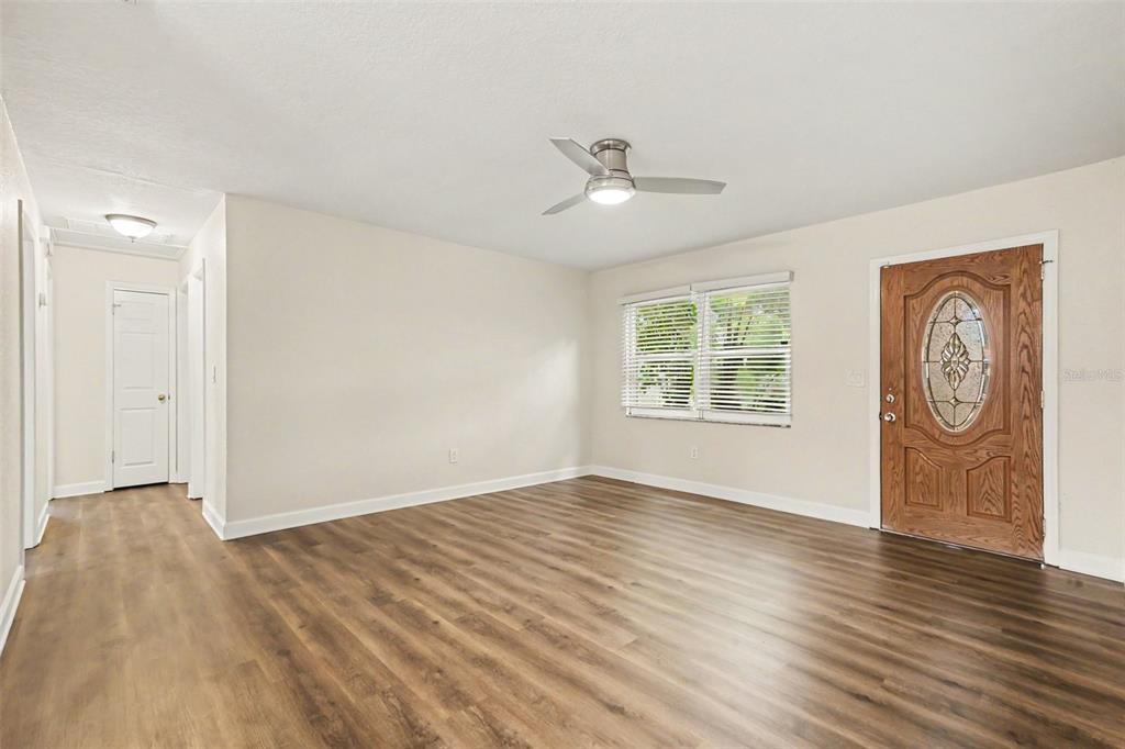 An empty room features light-colored walls, wood-look flooring, a ceiling fan, and a front door — 2051 23RD STREET SW, LARGO, FL