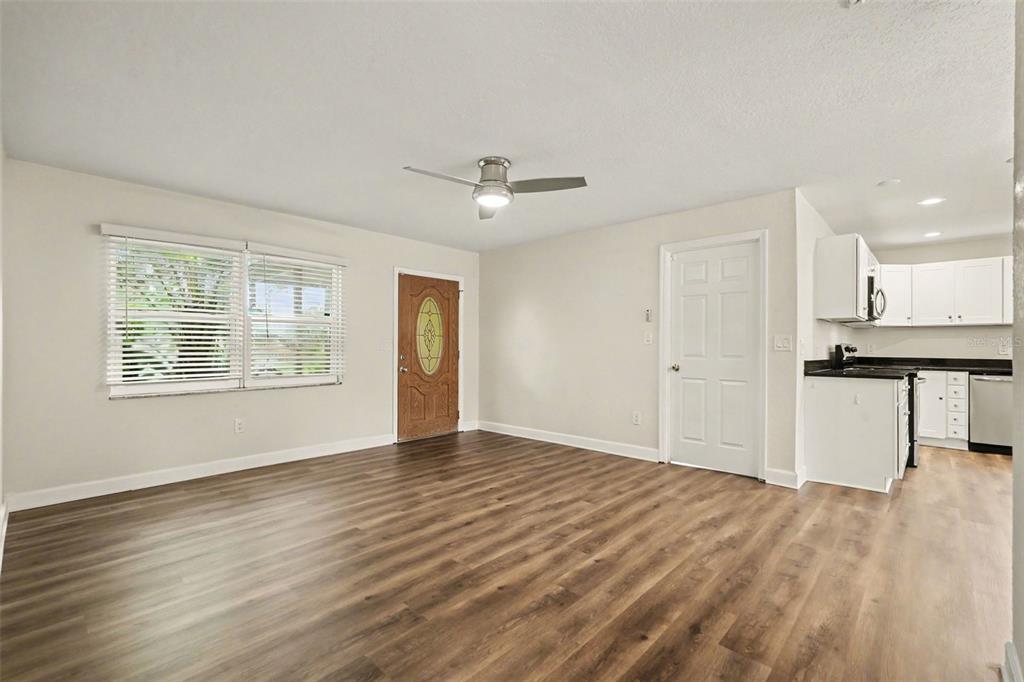 A living room with wood-look flooring, a ceiling fan, and an adjacent kitchen with white cabinets — 2051 23RD STREET SW, LARGO, FL