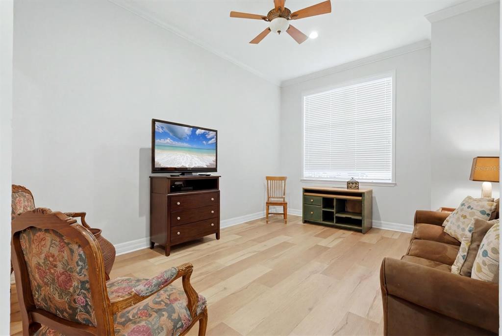A living room features light wood flooring, a ceiling fan, a television, and assorted furniture — 3409 54TH DRIVE W UNIT 103, BRADENTON, FL