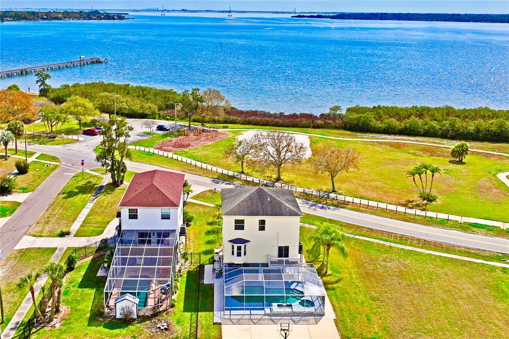 An aerial view shows a house with a pool cage near a park and water — 402 SHORE DRIVE W, OLDSMAR, FL