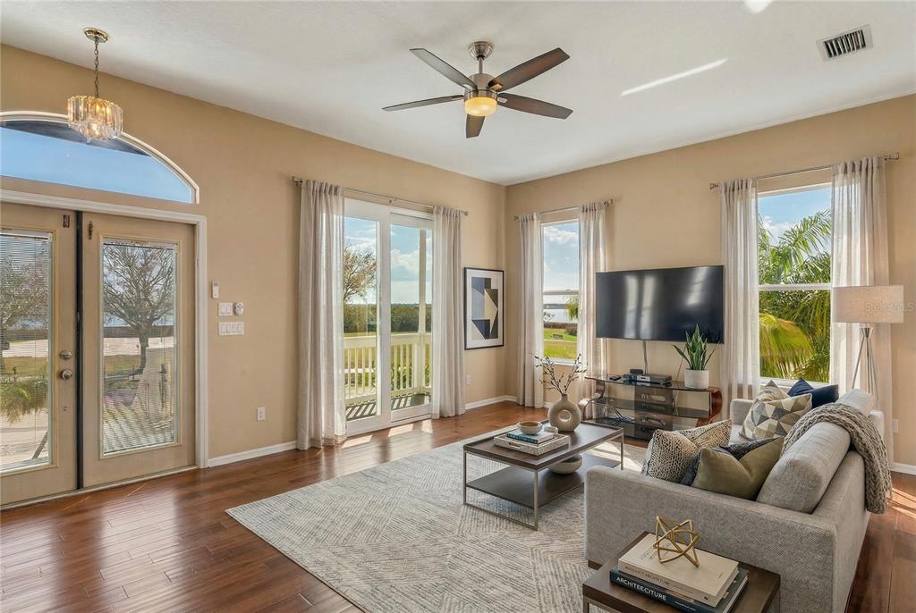 A living room features dark wood flooring, a ceiling fan, and sliding glass doors to a deck — 402 SHORE DRIVE W, OLDSMAR, FL
