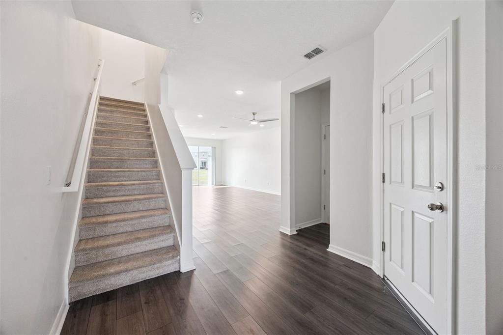 An entryway with a carpeted staircase, wood-look flooring, and a white front door — 759 SPRING PALMS LOOP, ORLANDO, FL