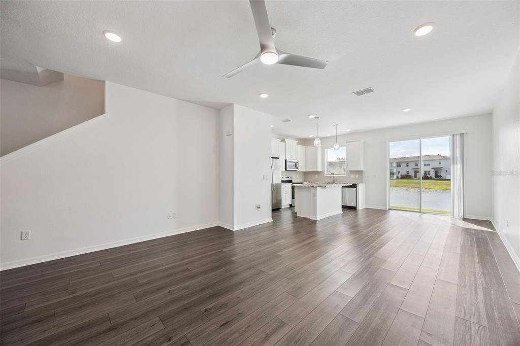An open-concept kitchen and living area features wood-look flooring, white cabinetry, and a sliding door — 759 SPRING PALMS LOOP, ORLANDO, FL