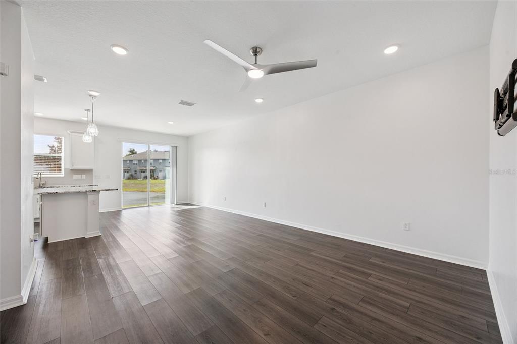 An open-concept living room features wood-look flooring, a ceiling fan, and an adjacent kitchen area — 759 SPRING PALMS LOOP, ORLANDO, FL