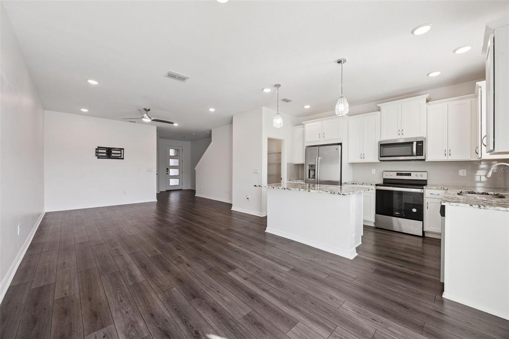 An open-concept kitchen and living area featuring white cabinets, granite countertops, and wood-look flooring — 759 SPRING PALMS LOOP, ORLANDO, FL
