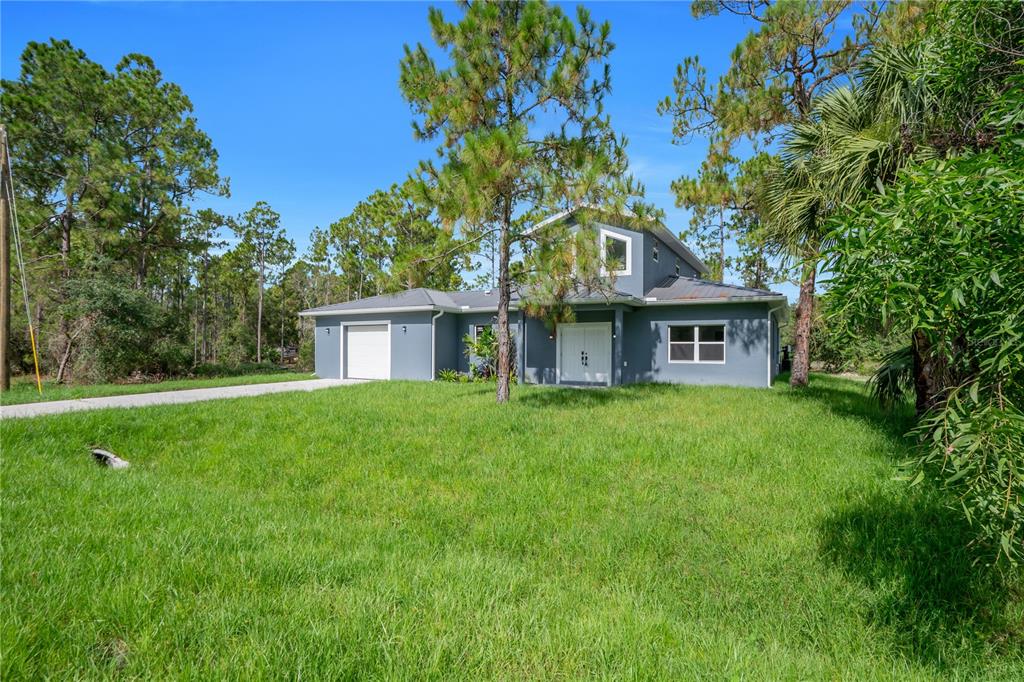 A two-story gray house with a metal roof and a single-car garage sits on grass — 317 JOHNS AVENUE, LEHIGH ACRES, FL