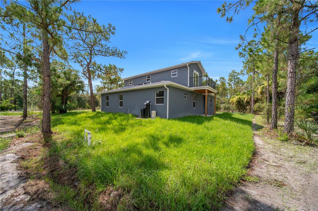 A two-story gray house with a balcony stands in a grassy, wooded lot — 317 JOHNS AVENUE, LEHIGH ACRES, FL