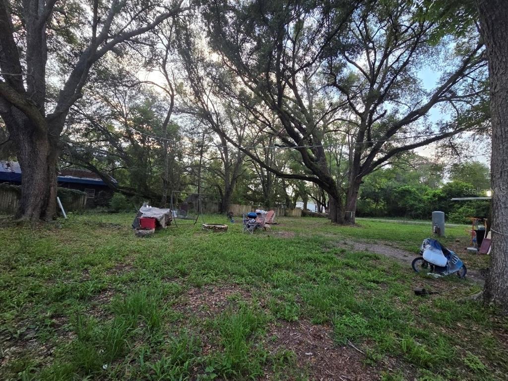 A grassy backyard features large oak trees, a fire pit, and scattered outdoor furniture — 7473 135TH CIRCLE, LIVE OAK, FL