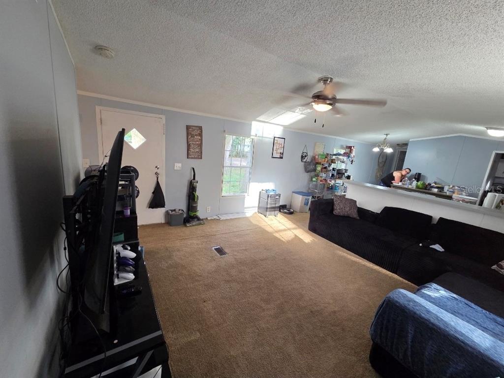 A living room features tan carpeting, a ceiling fan, and a large black sectional sofa — 7473 135TH CIRCLE, LIVE OAK, FL