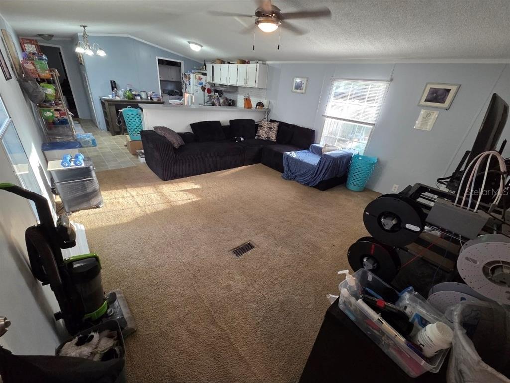 A living room with beige carpet, a black sectional sofa, and an open kitchen area — 7473 135TH CIRCLE, LIVE OAK, FL