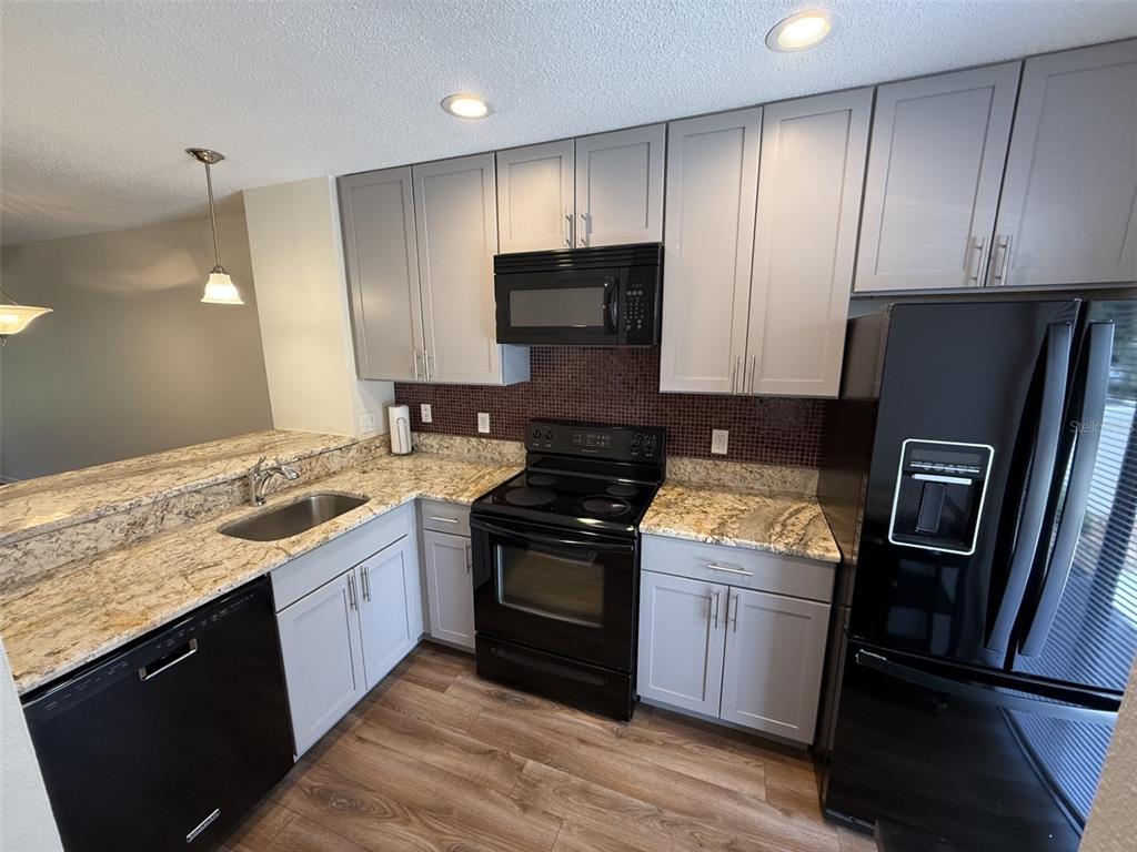 A kitchen features grey cabinets, granite countertops, black appliances, and a dark tiled backsplash — 819 OAK PARK PLACE, BRANDON, FL