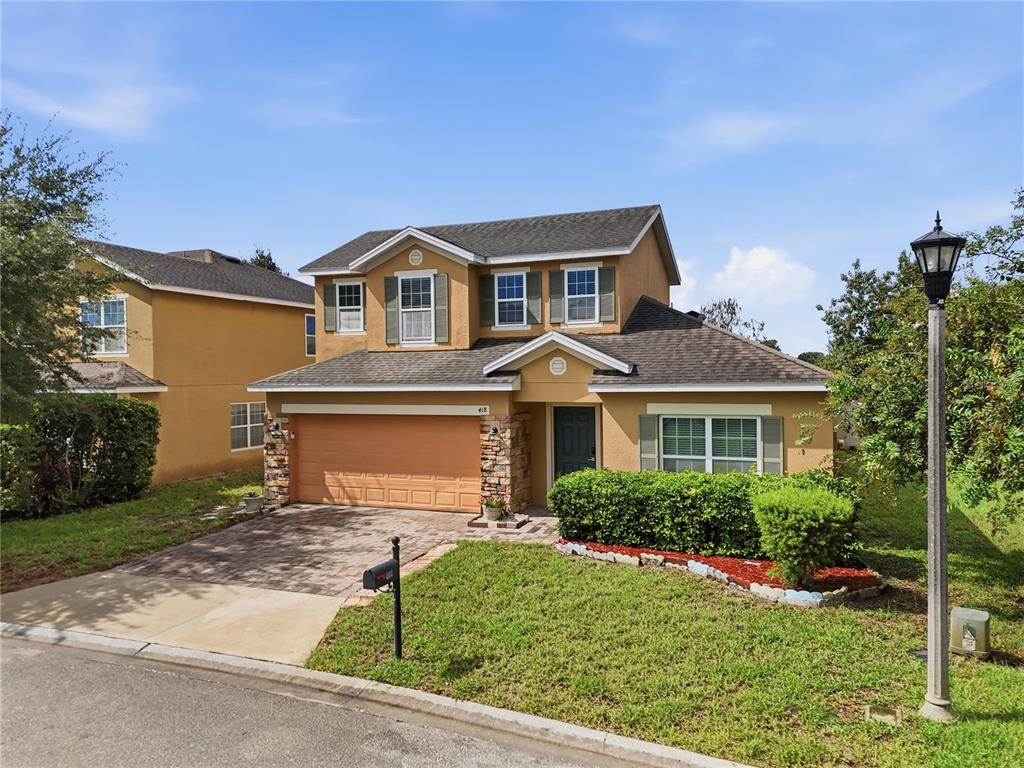 A two-story house with a tan exterior, stone accents, and a paved driveway — 418 VITORIA ROAD, DAVENPORT, FL