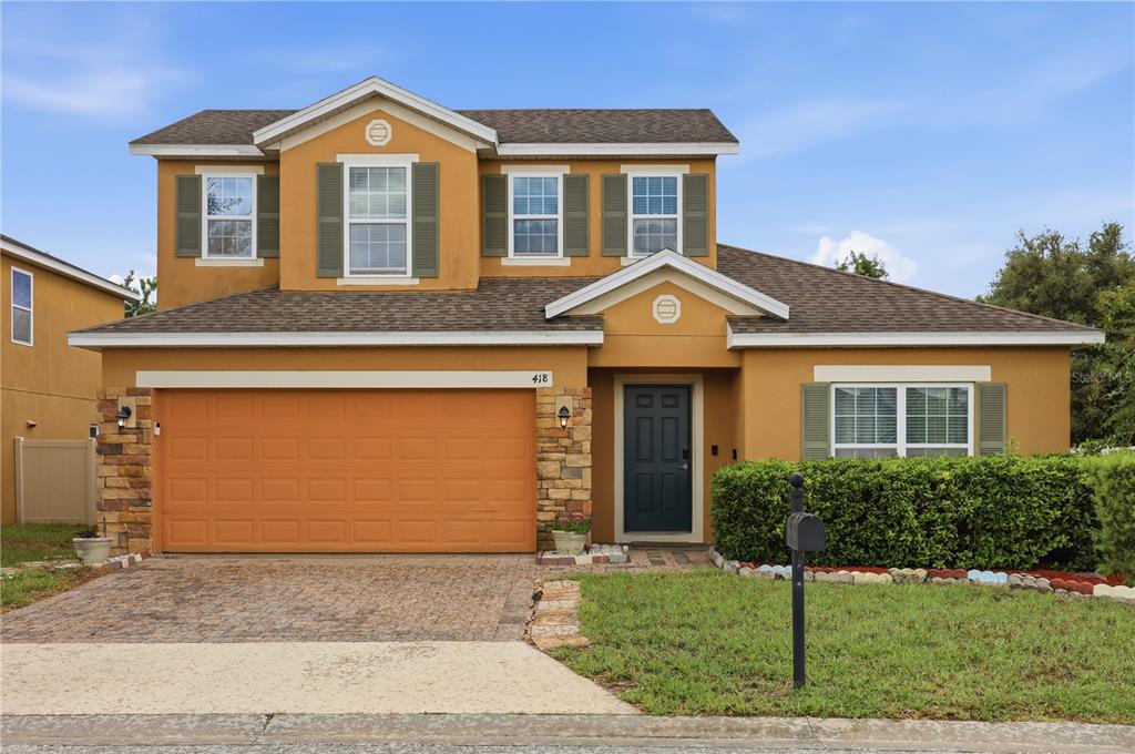 A two-story house with a tan stucco exterior, a two-car garage, and green shutters — 418 VITORIA ROAD, DAVENPORT, FL