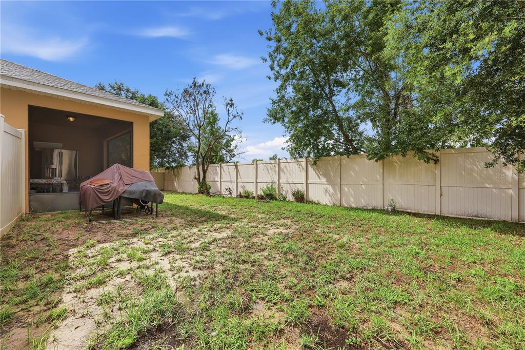 A backyard with a covered patio, a grill under a cover, and a vinyl privacy fence — 418 VITORIA ROAD, DAVENPORT, FL