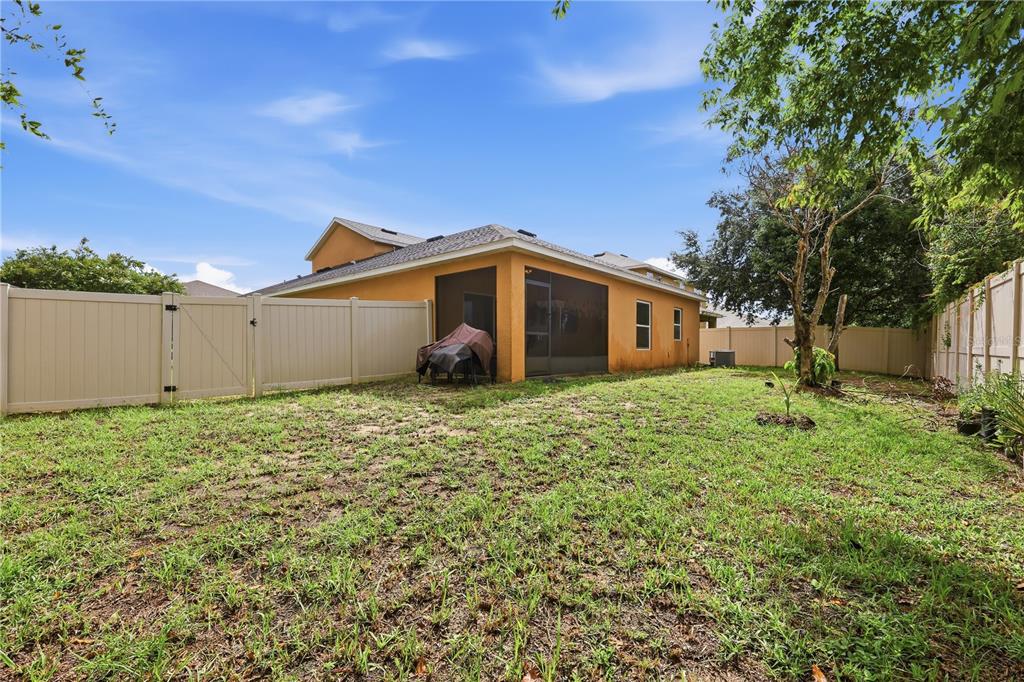 A backyard with a tan house, a screened-in porch, and a white vinyl privacy fence — 418 VITORIA ROAD, DAVENPORT, FL