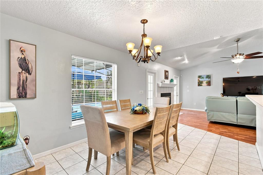 A dining area with a wooden table, chandelier, and tile flooring opens to a living room — 1009 SPRING LOOP WAY, WINTER GARDEN, FL