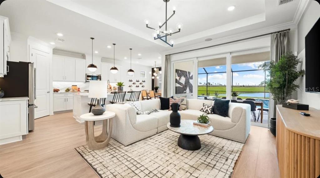 A modern white kitchen features a marble-topped island with black stools and pendant lighting — 7424 MOONBEAM AVENUE, SARASOTA, FL
