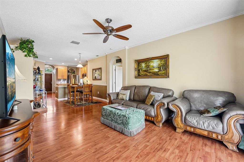 A living room with wood flooring, leather furniture, a green ottoman, and an open kitchen — 4236 TARKINGTON DRIVE, LAND O LAKES, FL