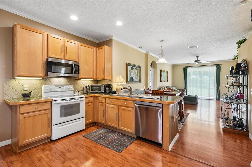 A kitchen with light wood cabinets, stainless steel appliances, and wood flooring opens to a dining area — 4236 TARKINGTON DRIVE, LAND O LAKES, FL