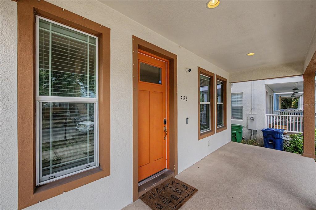 A covered front porch features a bright orange door and a welcome mat — 2126 W SPRUCE STREET, TAMPA, FL