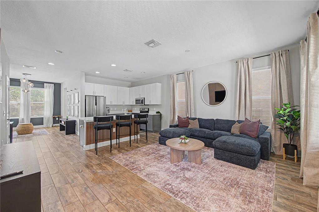 An open-concept living room and kitchen featuring wood-look tile flooring and a dark sectional sofa — 2126 W SPRUCE STREET, TAMPA, FL