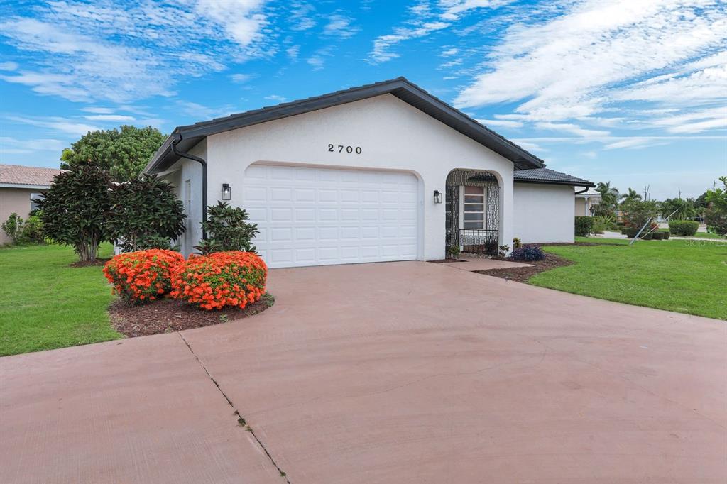 A single-story house with a white stucco exterior, a two-car garage, and orange flowering shrubs — 2700 W MARION AVENUE, PUNTA GORDA, FL
