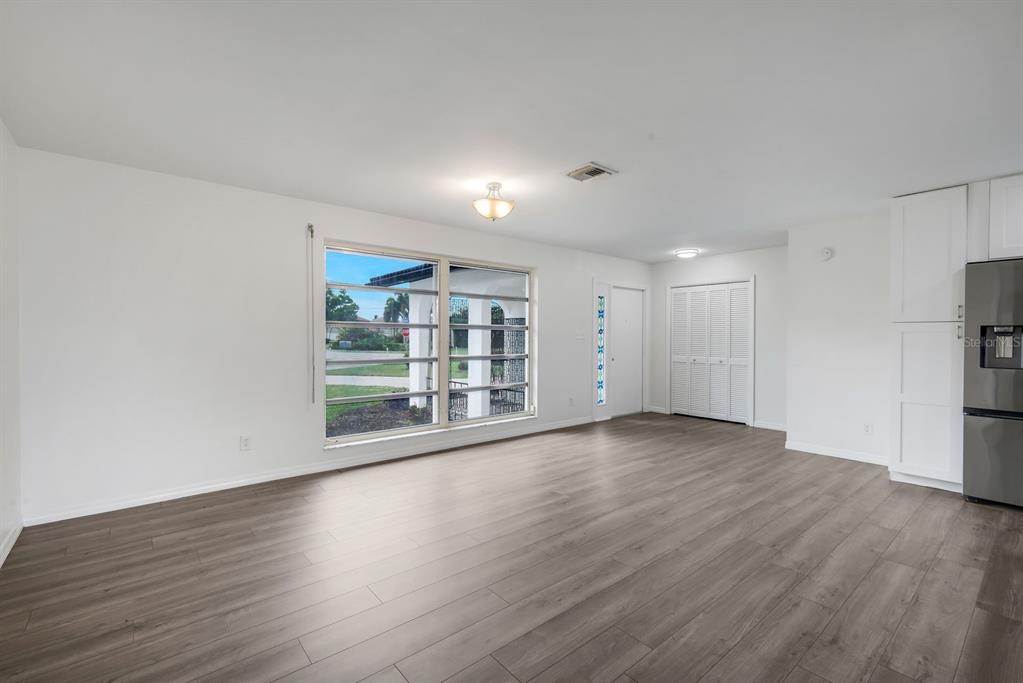 An empty room with light wood-look flooring, a large window, and white kitchen cabinetry — 2700 W MARION AVENUE, PUNTA GORDA, FL
