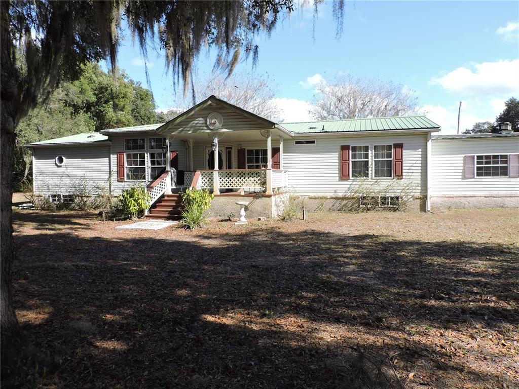 A single-story house with light siding, a green metal roof, and a front porch — 148 DENVER ROAD, CRESCENT CITY, FL