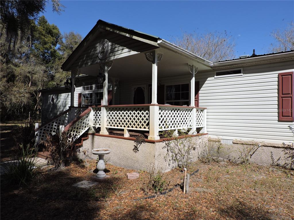 A single-story house with light siding, a covered front porch, and white lattice railings — 148 DENVER ROAD, CRESCENT CITY, FL