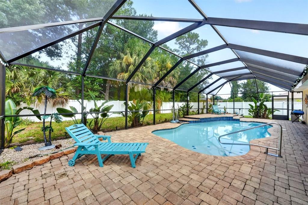 A screened-in patio features a swimming pool, brick pavers, and a blue lounge chair — 15 PINE CEDAR DRIVE, PALM COAST, FL