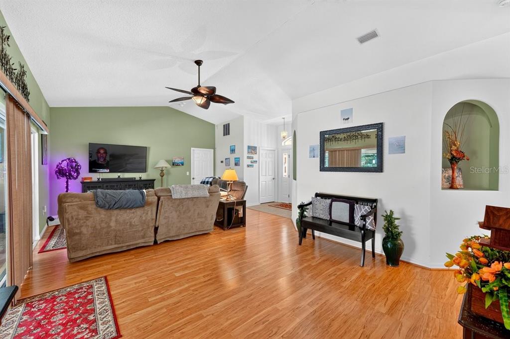 A living room with wood flooring, a vaulted ceiling, and an arched wall niche — 15 PINE CEDAR DRIVE, PALM COAST, FL