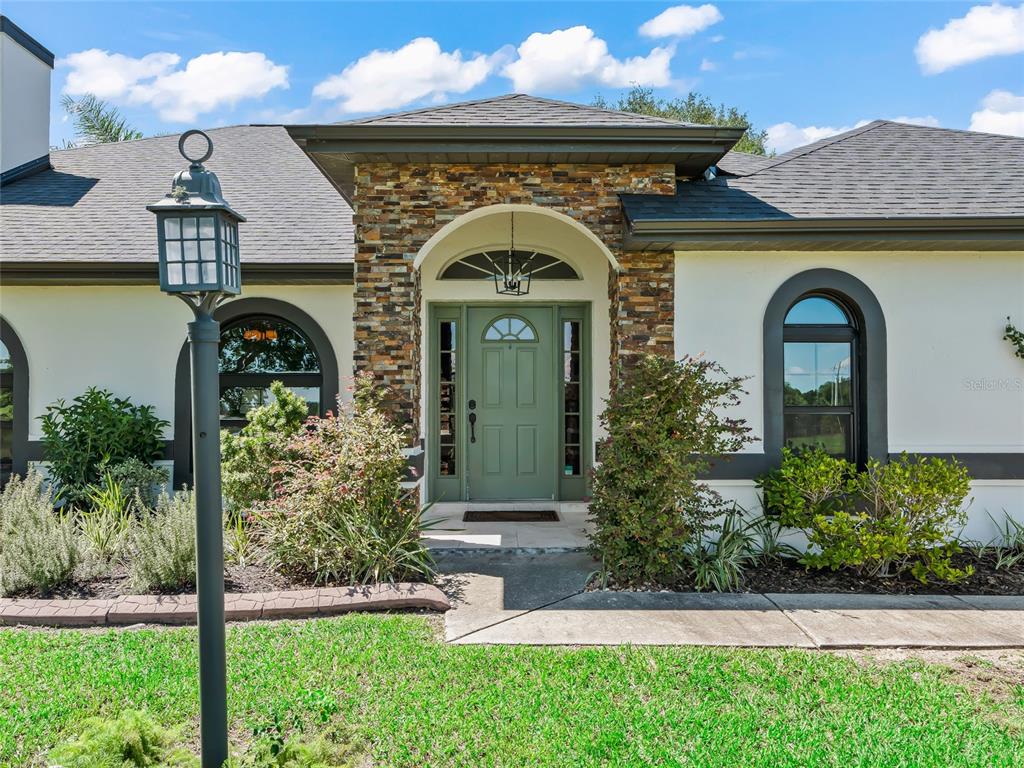 A single-story house with a stone-accented entryway, a green front door, and arched windows — 15600 SE 47TH AVENUE, SUMMERFIELD, FL