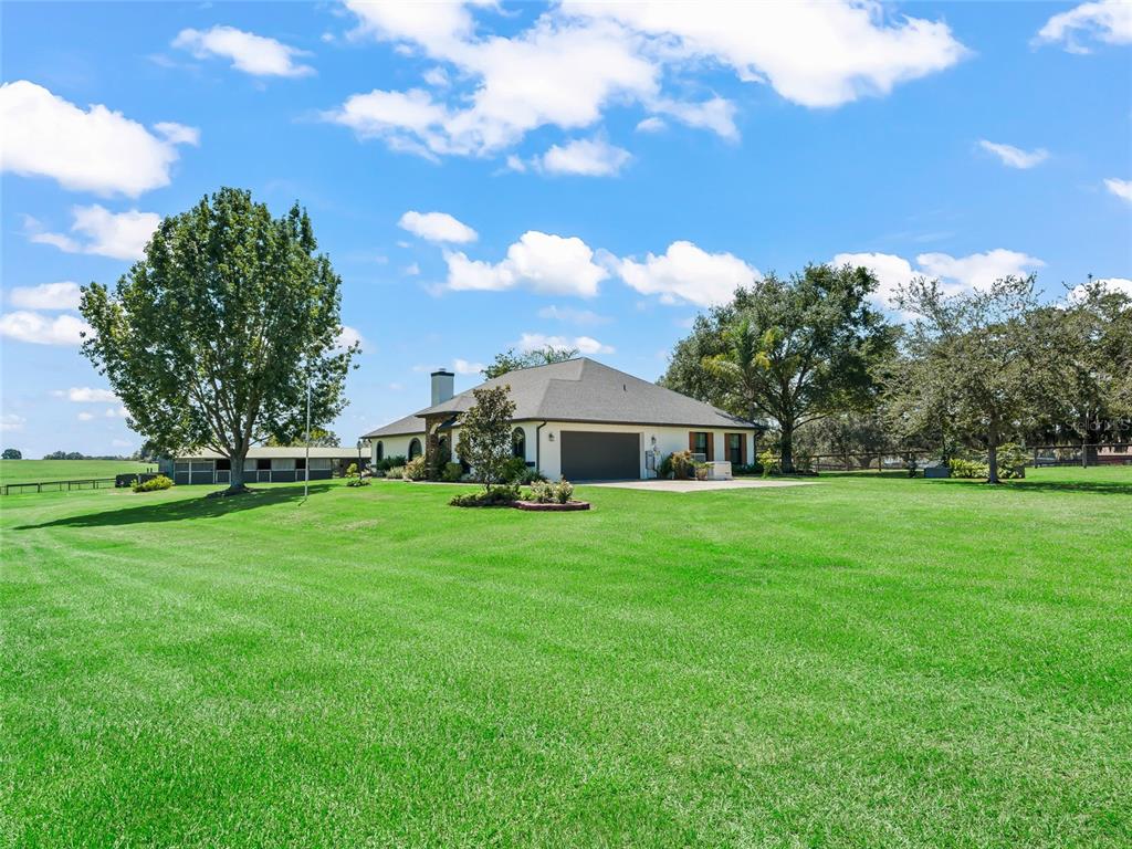 A single-story house with a garage sits on a large, grassy lot with trees — 15600 SE 47TH AVENUE, SUMMERFIELD, FL