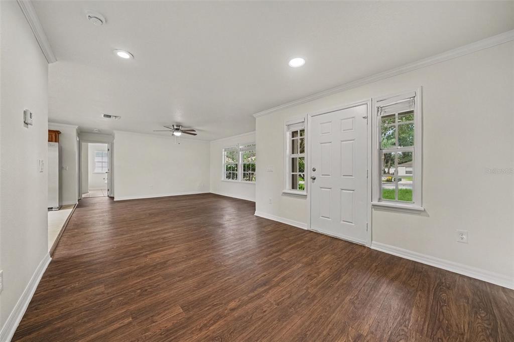 An empty living room with white walls, dark wood-look flooring, and a white front door — 245 OAK RUN COURT, APOPKA, FL