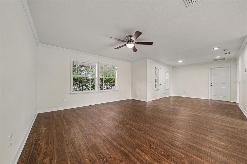An empty living room features dark wood-look flooring, white walls, and a ceiling fan — 245 OAK RUN COURT, APOPKA, FL