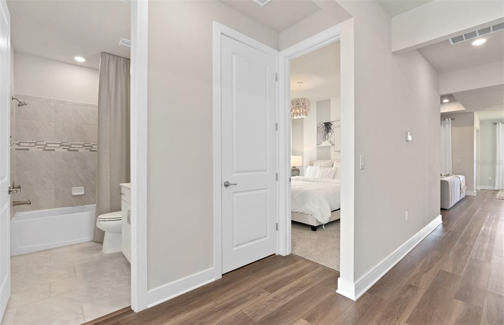 A hallway with wood-look flooring leads to a bathroom on the left and a bedroom — 2697 FERMOY DRIVE, ORMOND BEACH, FL
