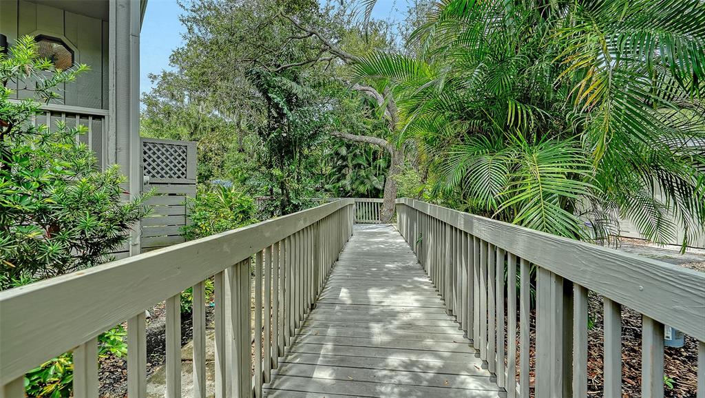 A wooden walkway with railings leads toward a lush, tree-filled outdoor area — 1372 LANDINGS POINT UNIT 28, SARASOTA, FL