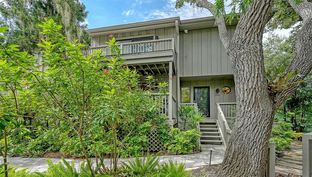 A two-story house with vertical siding features a balcony, a front porch, and mature trees — 1372 LANDINGS POINT UNIT 28, SARASOTA, FL