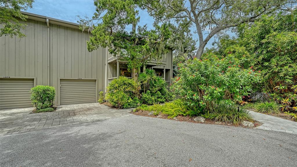 A two-story building with two garage doors and lush landscaping sits beside a paved driveway — 1372 LANDINGS POINT UNIT 28, SARASOTA, FL