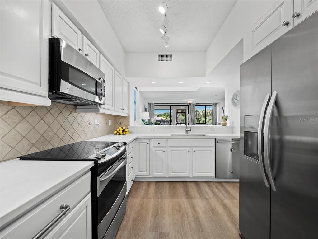 A white kitchen features stainless steel appliances, light wood-look flooring, and a view into the living area — 1906 HARBOURSIDE DRIVE UNIT 303, LONGBOAT KEY, FL