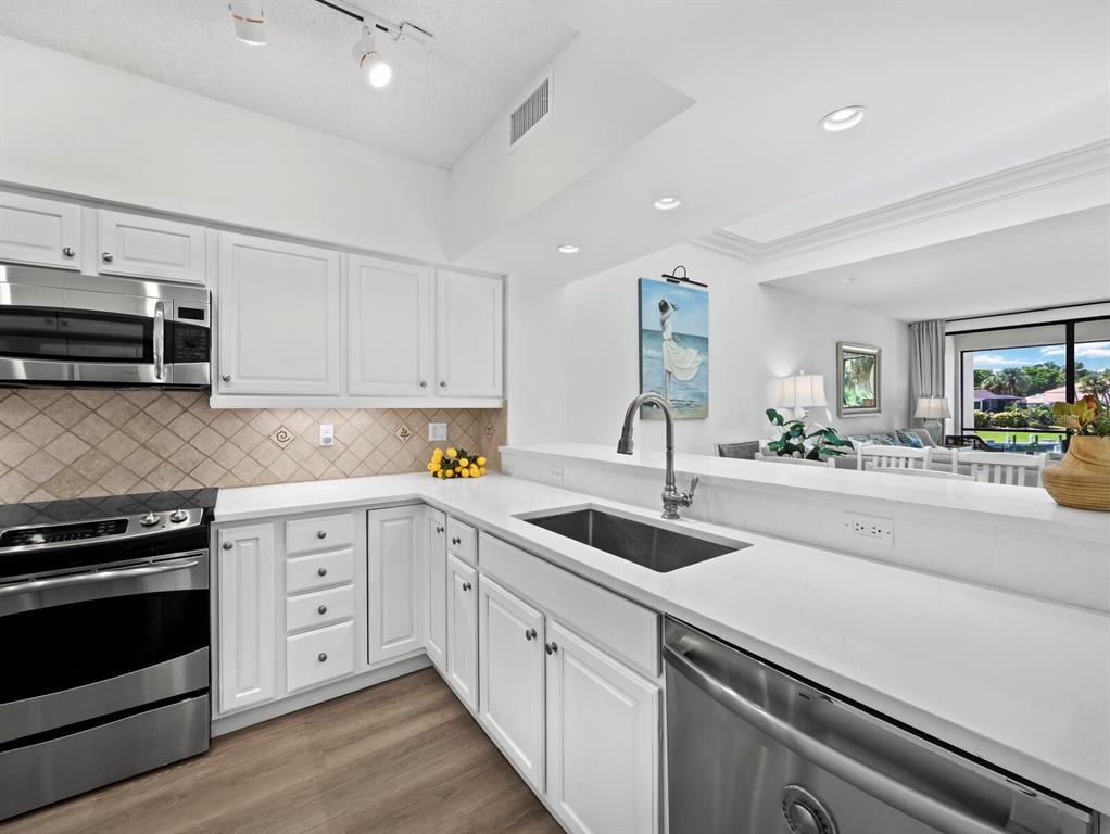 A white kitchen features stainless steel appliances, a farmhouse sink, and a breakfast bar — 1906 HARBOURSIDE DRIVE UNIT 303, LONGBOAT KEY, FL