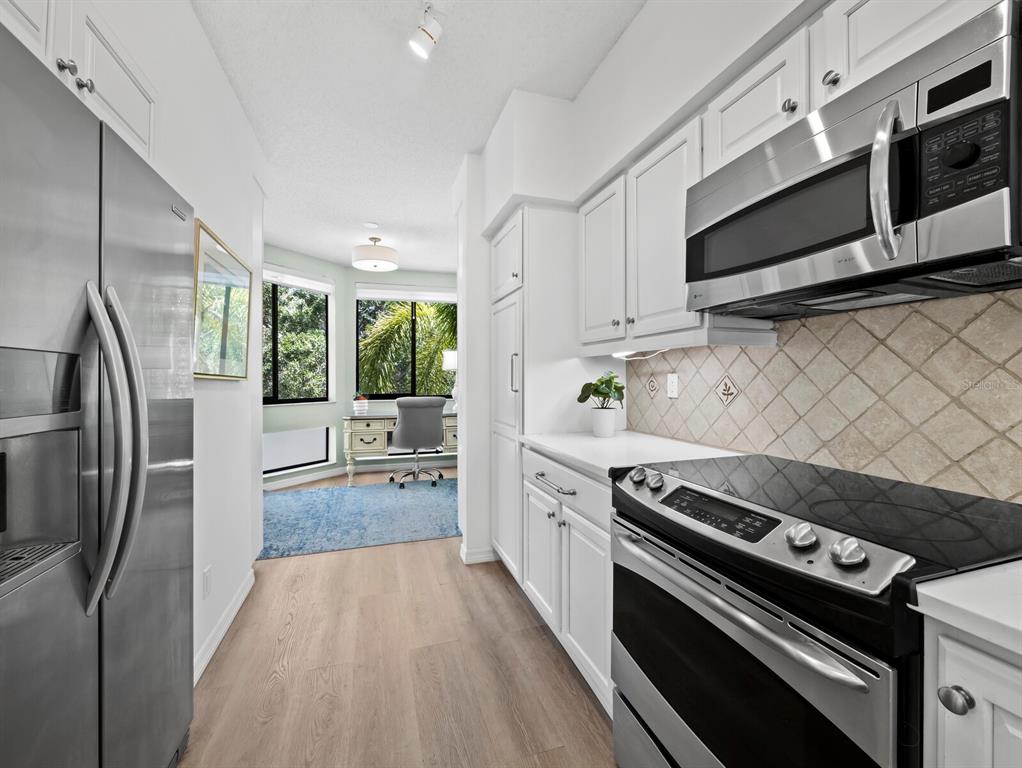 A galley kitchen with white cabinets and stainless steel appliances leads into a home office — 1906 HARBOURSIDE DRIVE UNIT 303, LONGBOAT KEY, FL