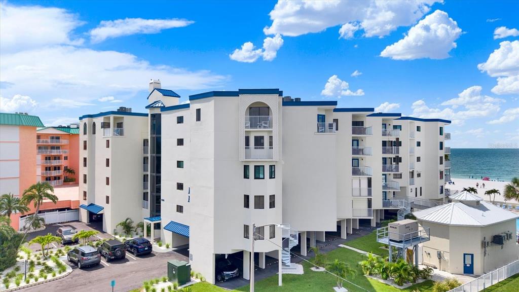 An exterior view of a multi-story white apartment building near the beach with parking — 18450 GULF BOULEVARD UNIT 213, INDIAN SHORES, FL