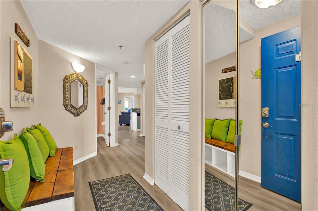 An entryway features a blue door, a wooden bench with green cushions, and mirrored closet doors — 18450 GULF BOULEVARD UNIT 213, INDIAN SHORES, FL