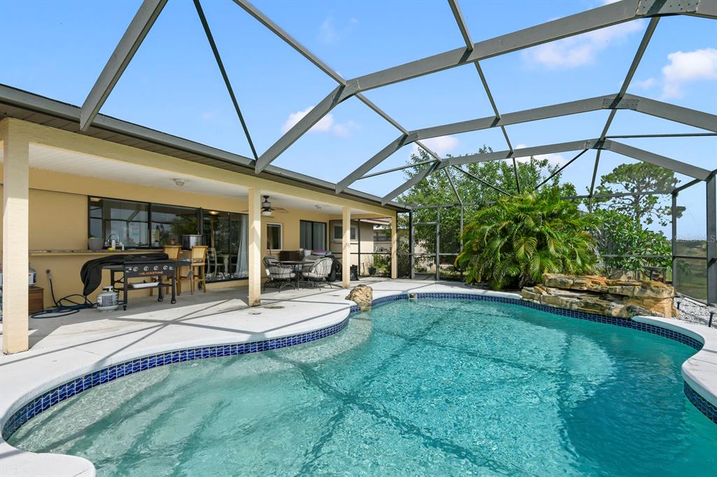 A screened-in patio features a swimming pool with a rock waterfall and a grill area — 744 FLAMINGO DRIVE, APOLLO BEACH, FL