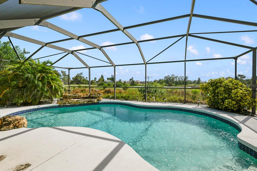 A screened-in swimming pool with a rock waterfall feature overlooks a grassy outdoor area — 744 FLAMINGO DRIVE, APOLLO BEACH, FL